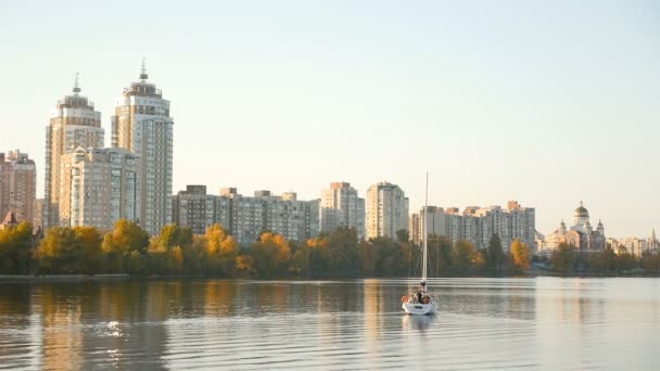 Un yate de vela blanca flota en el río contra el telón de fondo de hermosas casas. Movimiento lento — Vídeos de Stock