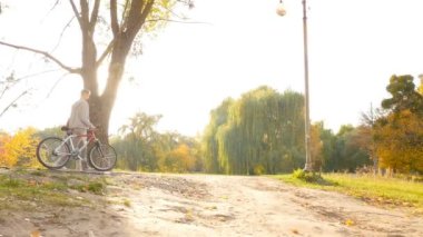 Guy with the girl are walking in the autumn Cyty park. Bicycle rides. Slow motion. 10.15.2019 Ukraine. Kiev VDNH
