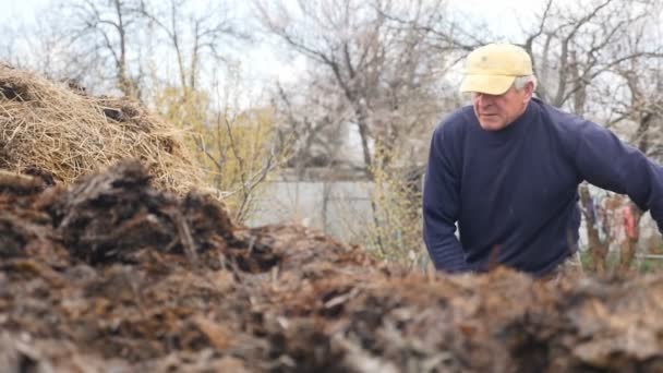 Muž ve žluté čepici hodí trus vidlemi. Venkov. Zpomalený pohyb — Stock video