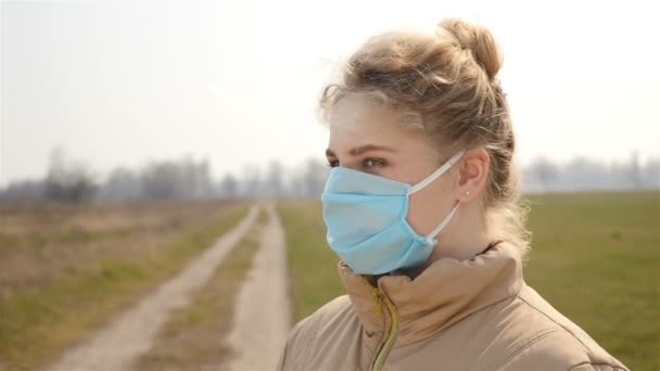 Una chica con una máscara médica se vuelve hacia la cámara. Movimiento lento — Vídeos de Stock