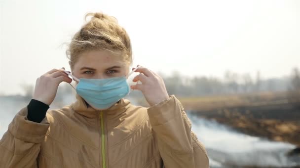 Upprörd flicka tar på sig en medicinsk mask. Rökfält. Bränt gräs. Miljöförstöring. Sakta i backarna. Närbild — Stockvideo