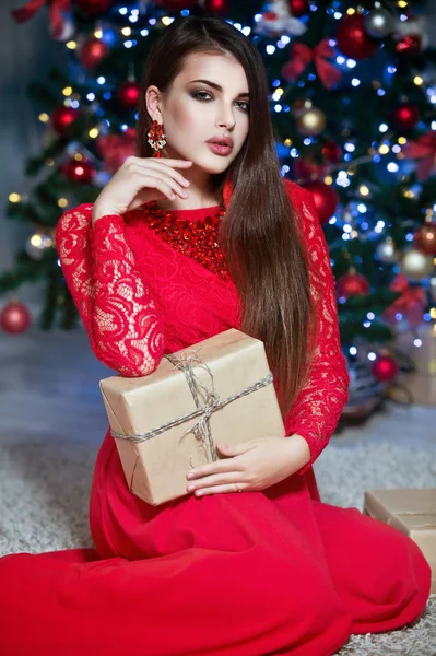 Woman with christmas box gift near red white Christmas tree.