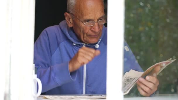 Vieil homme lit et ajuste les lunettes au rebord de la fenêtre vue de près — Video