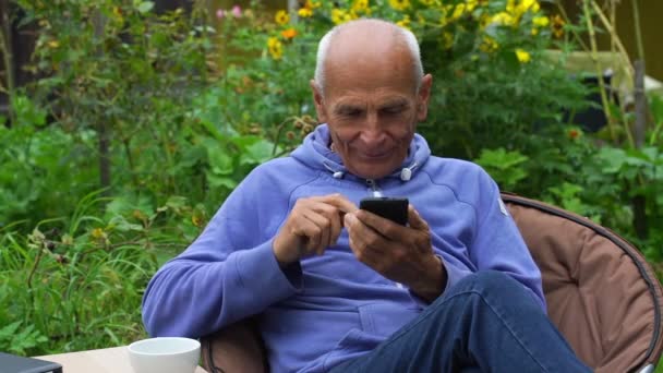 Пенсіонер приймає телефонний дзвінок пити чай в саду крупним планом — стокове відео
