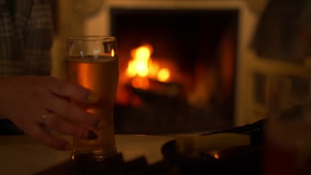 Mulher embaçada leva copo de cerveja da mesa contra lareira — Vídeo de Stock