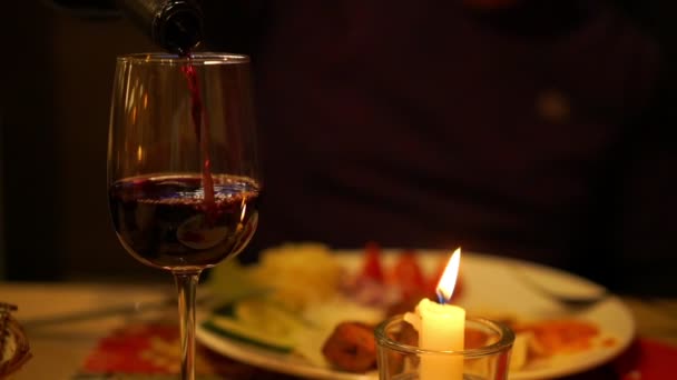 Человек наливает вкусное красное вино в бокал при свечах крупным планом — стоковое видео