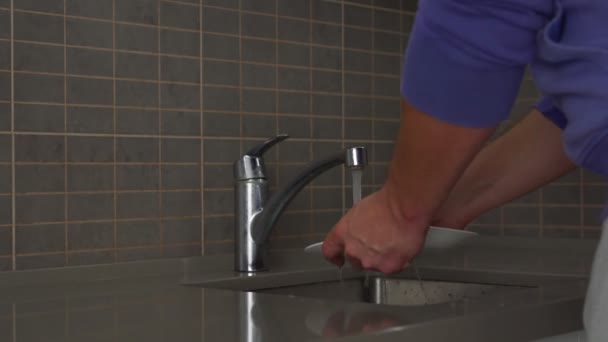 Человек в пуловере моет тарелку в кухонной раковине с губкой — стоковое видео