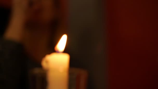 Воскова свічка полум'я проти розмитої жінки з келихом — стокове відео