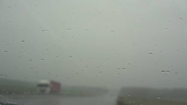 Arabanın ön camına küçük yağmur damlaları düşer ve silecekler hareket eder.