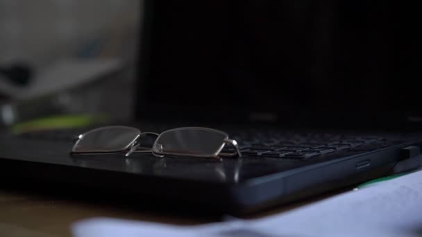 Transparent glasses for vision lie on black laptop surface — Stock Video