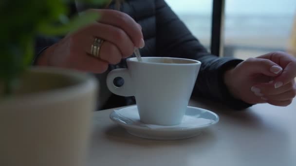 Kvinna i svart jacka rör socker i vit kaffekopp nära — Stockvideo