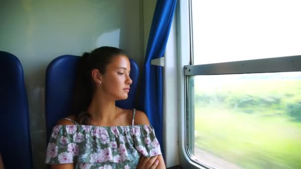 Girl yawns and falls asleep in train passing landscape — Stock Video