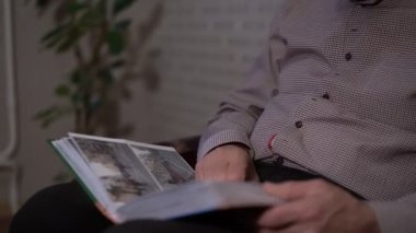 Kareli tişört giyen emekli adamın kalın bir fotoğraf albümü var.