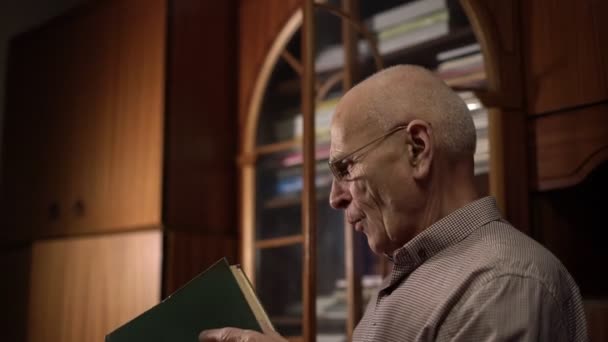 Senior homme dans des lunettes détient grand livre vert soufflant la poussière — Video