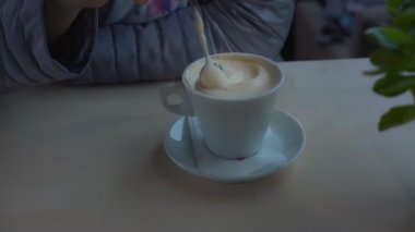 Manikürlü kadın espresso üzerine yoğun süt köpüğü karıştırıyor.