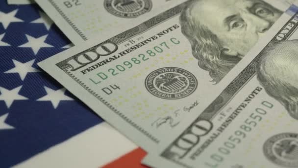 Billetes de cien dólares se encuentran en primer plano de la bandera estadounidense giratoria — Vídeo de stock
