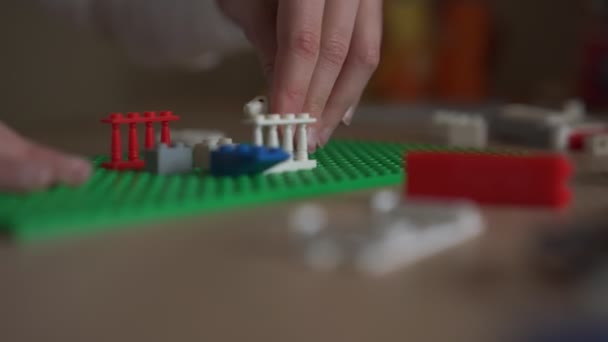 Девушка устанавливает большие пластиковые элементы Лего на зеленую платформу — стоковое видео