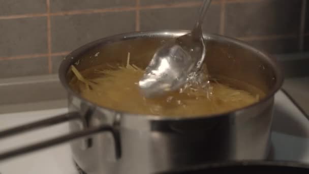 Persoon hand roert spaghetti met lepel in kokend water — Stockvideo