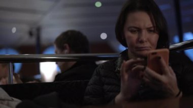 Kadın feribot kafesinde oturuyor ve telefonla internette sörf yapıyor.