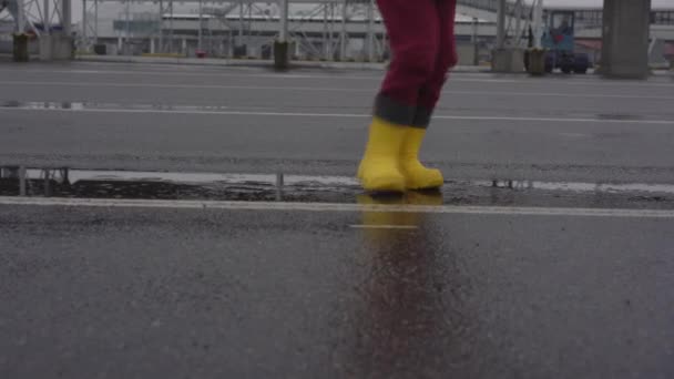 Funny child in yellow waterproof rubber boots enjoys jumping — Stock Video