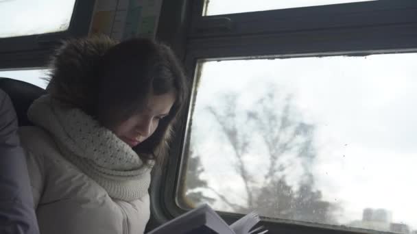 Chica va en tren eléctrico y lee libro sentado en la ventana — Vídeo de stock