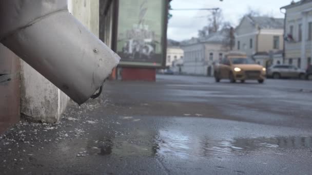 El agua del techo gotea por la tubería de drenaje en el camino asfaltado de la ciudad — Vídeos de Stock