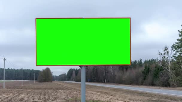 Рекламный щит с зеленым экраном, расположенный рядом с серой асфальтовой дорогой — стоковое видео