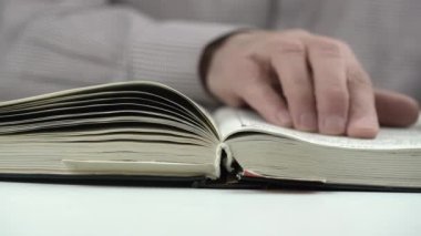 Tişörtlü yaşlı adam büyük bir kitap sayfası okuyor ve parmaklarını çalıştırıyor.