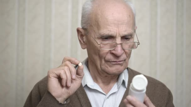 Senior homme avec des lunettes regarde bouteille de pilules dans la chambre — Video