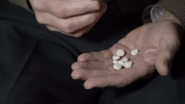 Beceriksiz elleri olan yaşlı bir adam avuç içlerine hap koyar.