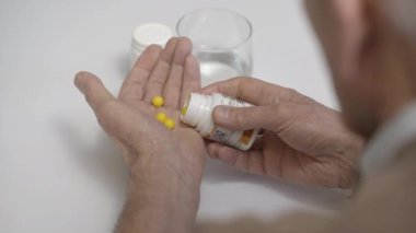 Olgun adam masanın üstündeki plastik kavanozdan sarı haplar alıyor.