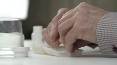 Yaşlı adam buruşuk elleri parlak sarı tabletleri ayırır.
