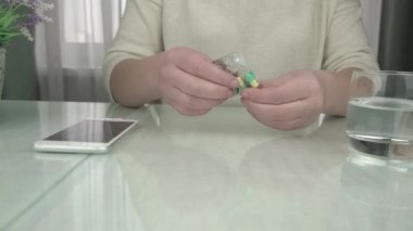 Beyaz kazaklı kadın renkli haplar alıyor ve su içiyor.