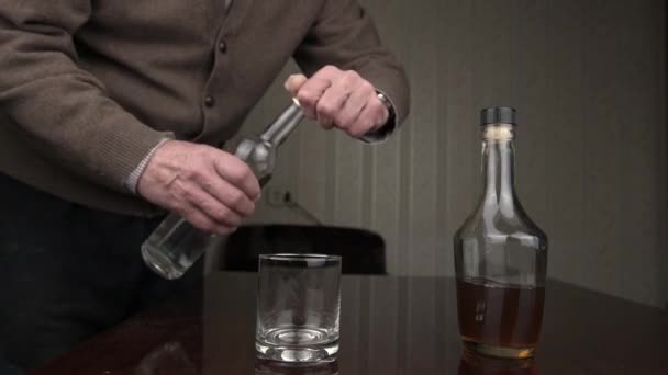 Gerijpte man giet alcohol in glas en zit op zwarte stoel — Stockvideo