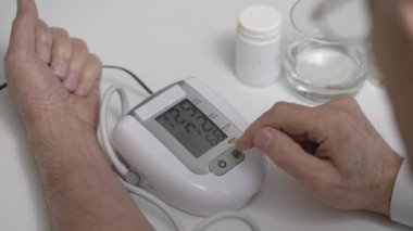 Yaşlı adam kan basıncını monitörle ölçüyor.