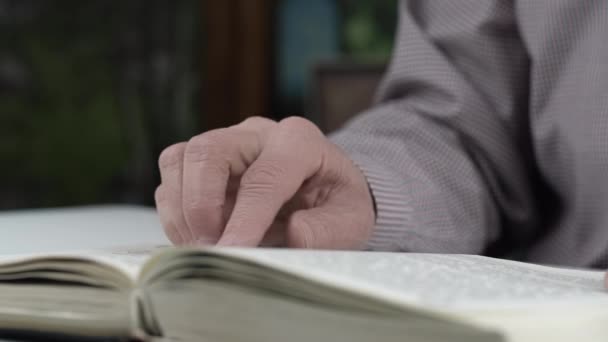 O homem sênior na camisa checkered lê o dedo do deslizamento do livro — Vídeo de Stock