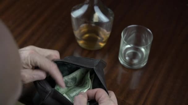 Gepensioneerde kijkt naar bankbiljetten in portemonnee en drinkt cognac — Stockvideo