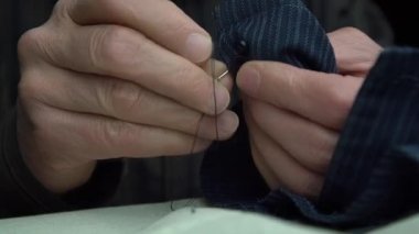 terzi siyah düğme dikmeyi bitiriyor ipliği yakın plan kesiyor