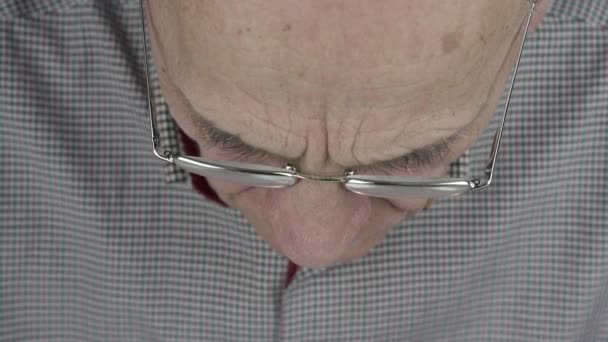 Концентрированный пожилой человек в очках смотрит вниз — стоковое видео
