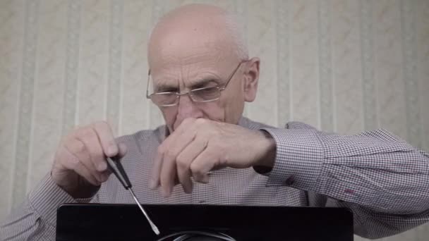 Old man in glasses screws black TV set detail at home — Stock Video