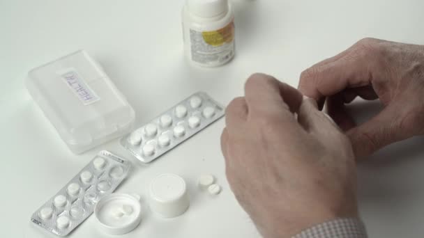 Senior man zet kleine witte pillen in plastic containers — Stockvideo