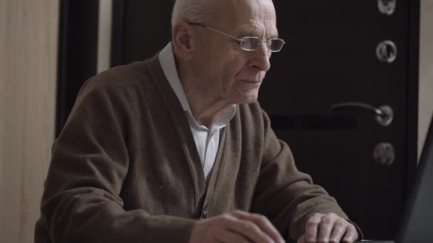 Hombre mayor se sienta en la computadora inalámbrica y trabaja en la jubilación — Vídeo de stock
