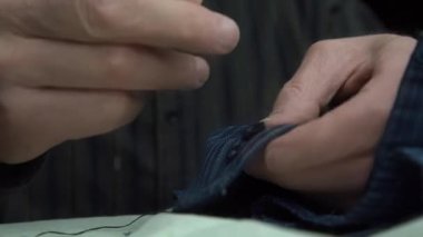 Yaşlı adam gömlek kollarına iplik kullanarak küçük düğmeler dikiyor.