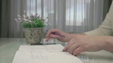 İş kadını defter sayfasına yazı yazıyor. Masada oturuyor.