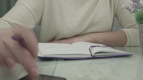 Jonge vrouw in pullover schrijft in notebook met paarse pen — Stockvideo