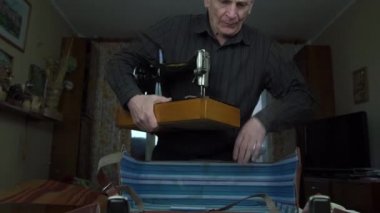 Adam dikiş makinesini bavuldan çıkarıp masaya koyuyor.