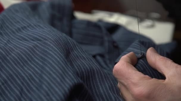 Старик пришивает пуговицу ниткой и иглой к рубашке — стоковое видео