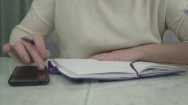 Genç kadın akıllı telefona güveniyor ve not defterine yazıyor.