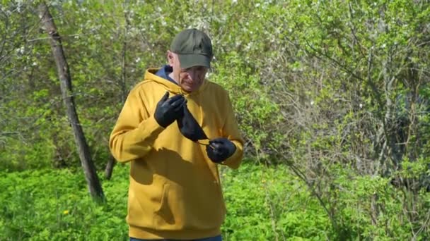 म्हातारा माणूस हिरव्या झाडांमध्ये काळा डिस्पोजेबल मास्क ठेवतो — स्टॉक व्हिडिओ