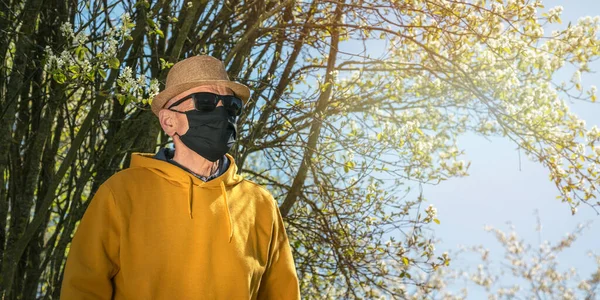 Velho homem de máscara descartável preto fica perto da árvore do jardim — Fotografia de Stock